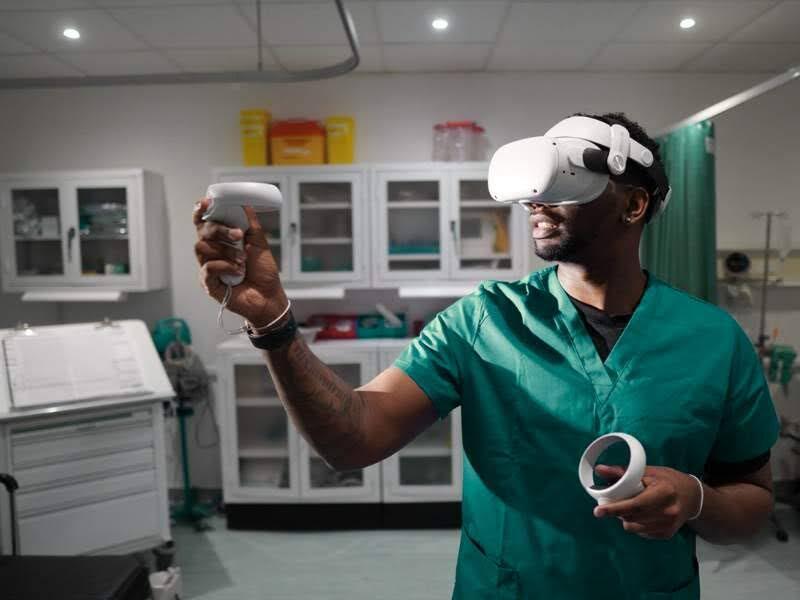 A photo of a man in nurse scrubs wearing a VR headset and holding two white VR remotes. 