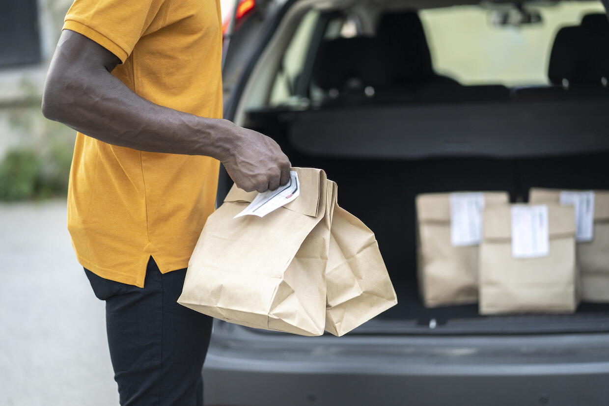 A person carrying paper bags with other paper bags placed in the open trunk of a car.