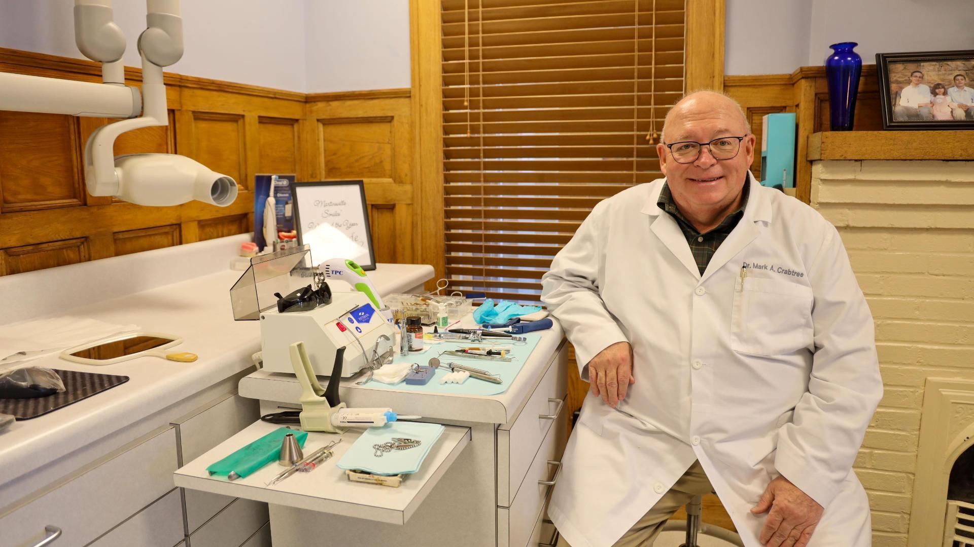 A photo of a man sitting next to a table of dental equipment. 