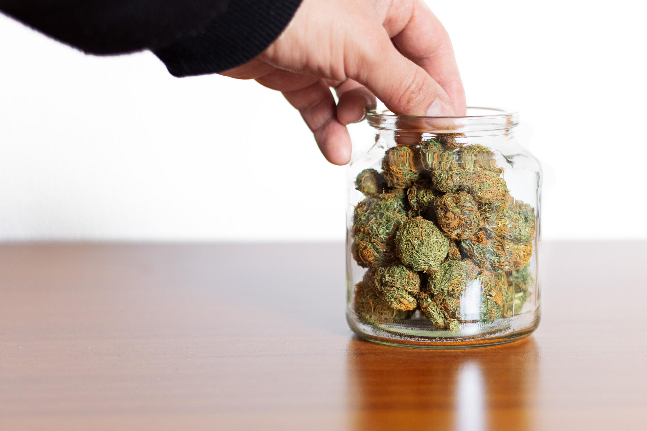 A photo of a hand reaching into a jar full of marijuana nuggets. 