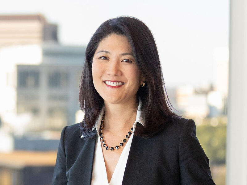 A portrait of a woman from the waist up standing in front of a window. 