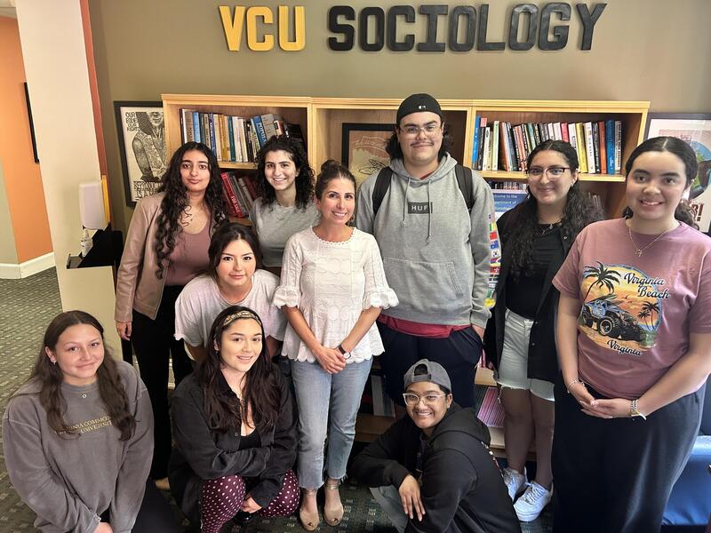 A group photo of 10 people in front of a book case. Above the bookcase are letters on a wall that spell out \"VCU SOCIOLOGY\"