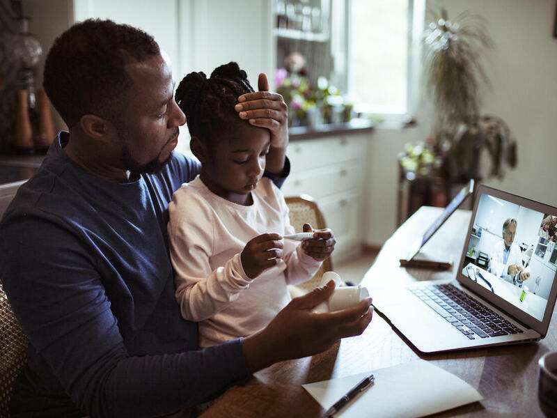 A father and daughter participate in a virtual telemedicine meeting.