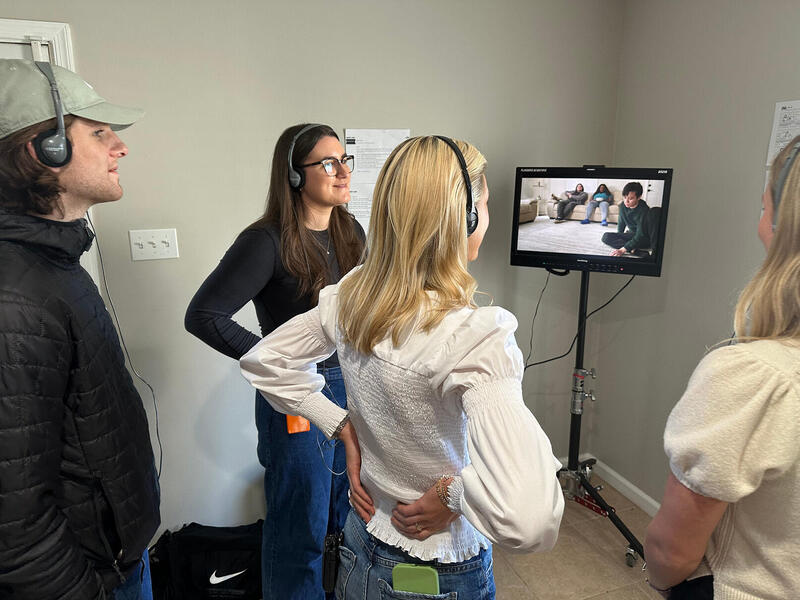 A photo of four people standing in a room looking at a screen