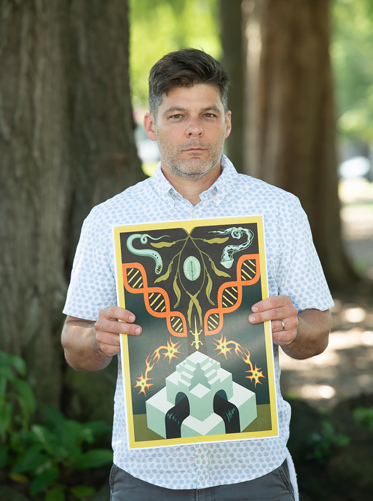 Biology professor Chris Gough, Ph.D., stands in Monroe Park while holding a piece of art produced by one of his students.