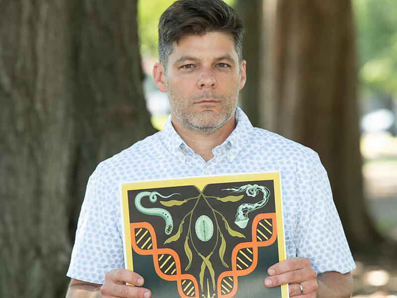 Biology professor Chris Gough, Ph.D., stands in Monroe Park while holding a piece of art produced by one of his students.