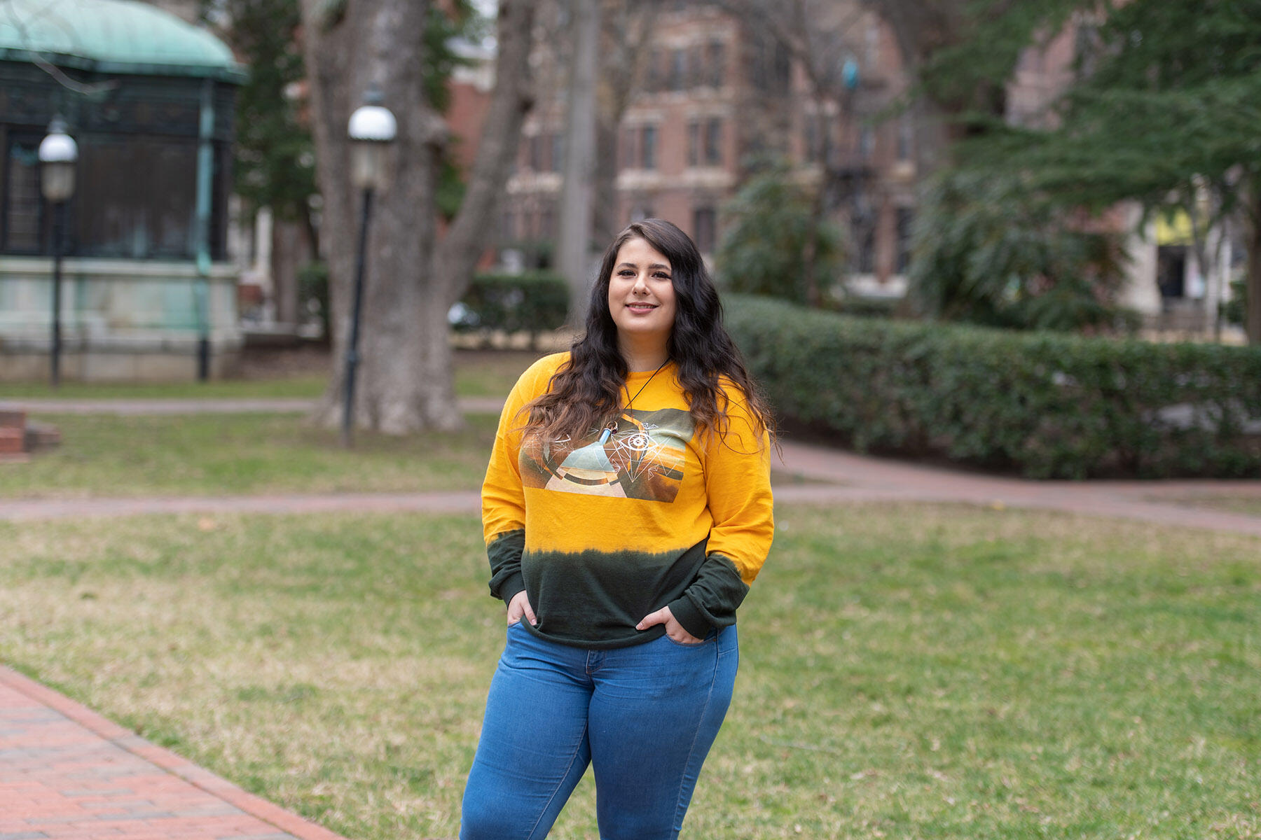 Woman in yellow shirt standing with hands in pockets.