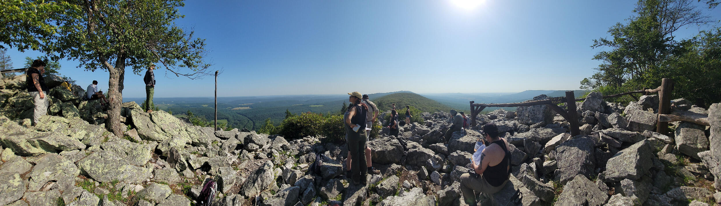 People are spread across a scenic rocky mountain lookout.