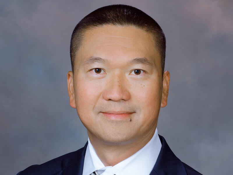 A photo of a man from the shoulders up. He is wearing a suit and tie. 