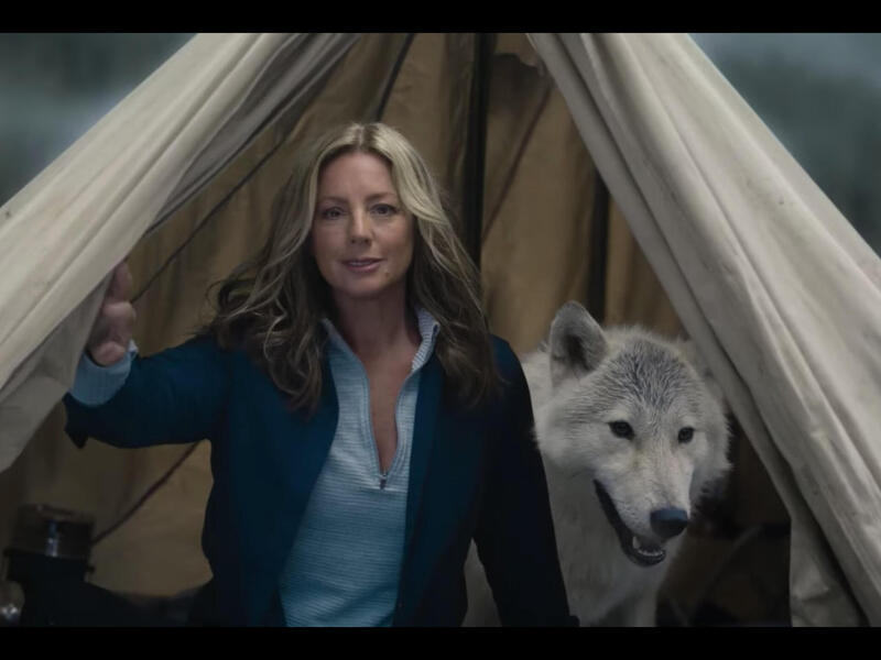 A woman standing in the middle of an open tent with a white and gray wolf standing behind her. 