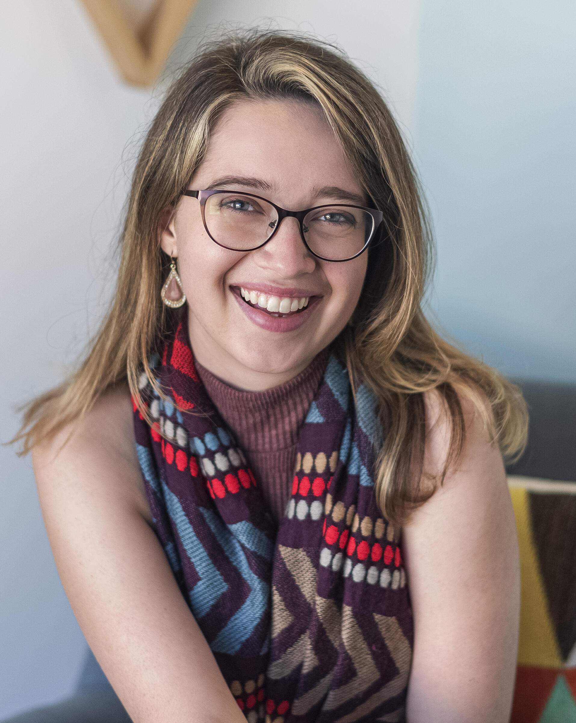 A portrait of a blond woman wearing a multi colored scarf and purple glasses. 