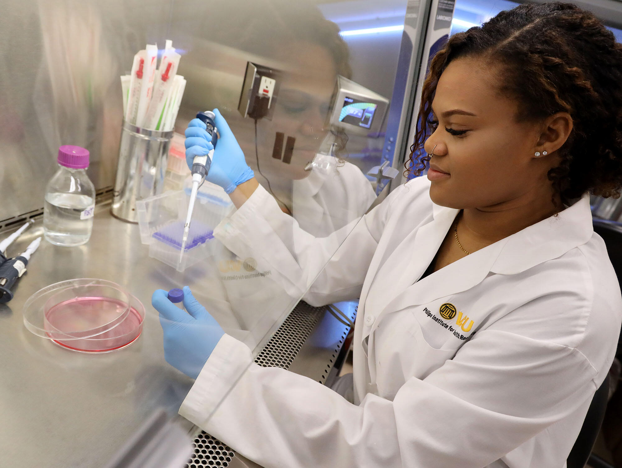 A woman wearing a lab coat filling a test tube with liquid. 