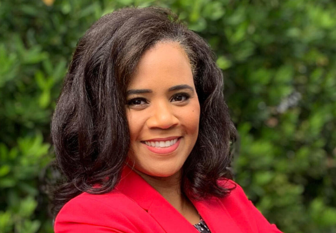 A photo of a smiling woman with her arms crossed against her chest. 