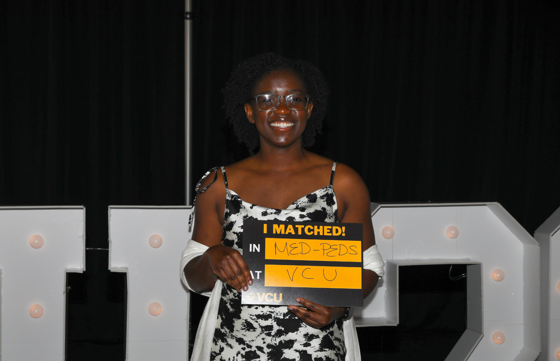 A photo of a woman holding a sign that says \"I MATCHED!\" \"IN MED-PEDS\" \"AT VCU\"