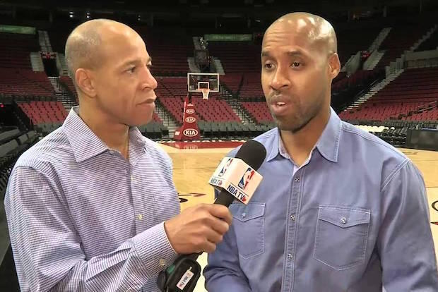 Two people standing. One is holding a microphone for the other.