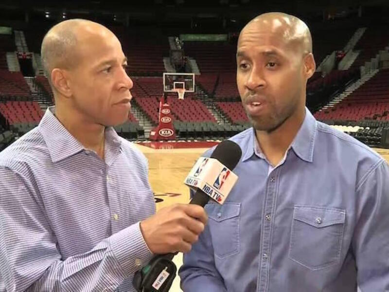 Two people standing. One is holding a microphone for the other.