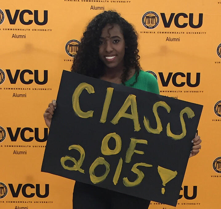 A woman smiles and holds a handwritten sign that says Class of 2015.