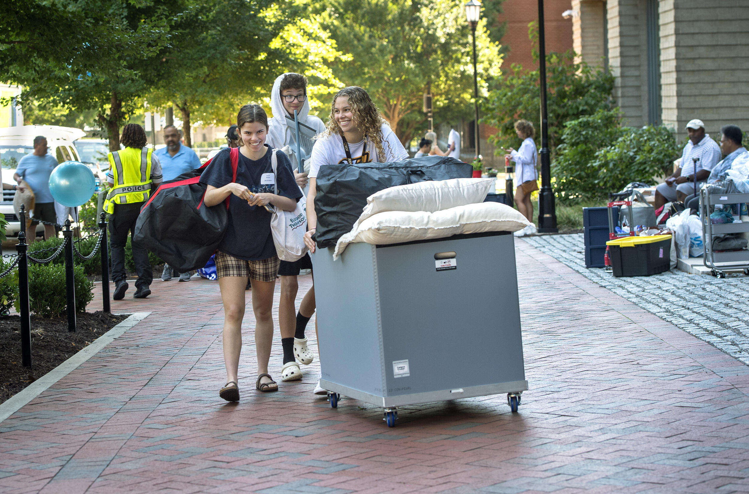A woman pushing a bin with pillows coming out of it with another woman next to her and a man behind her. 