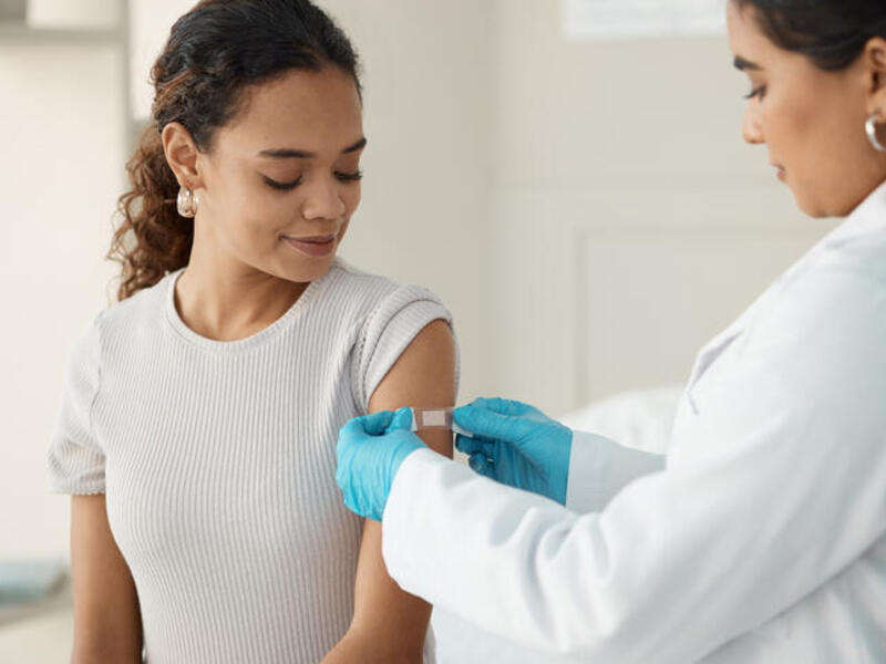A photo of a doctor putting a bandaid on a woman's upper arm. 
