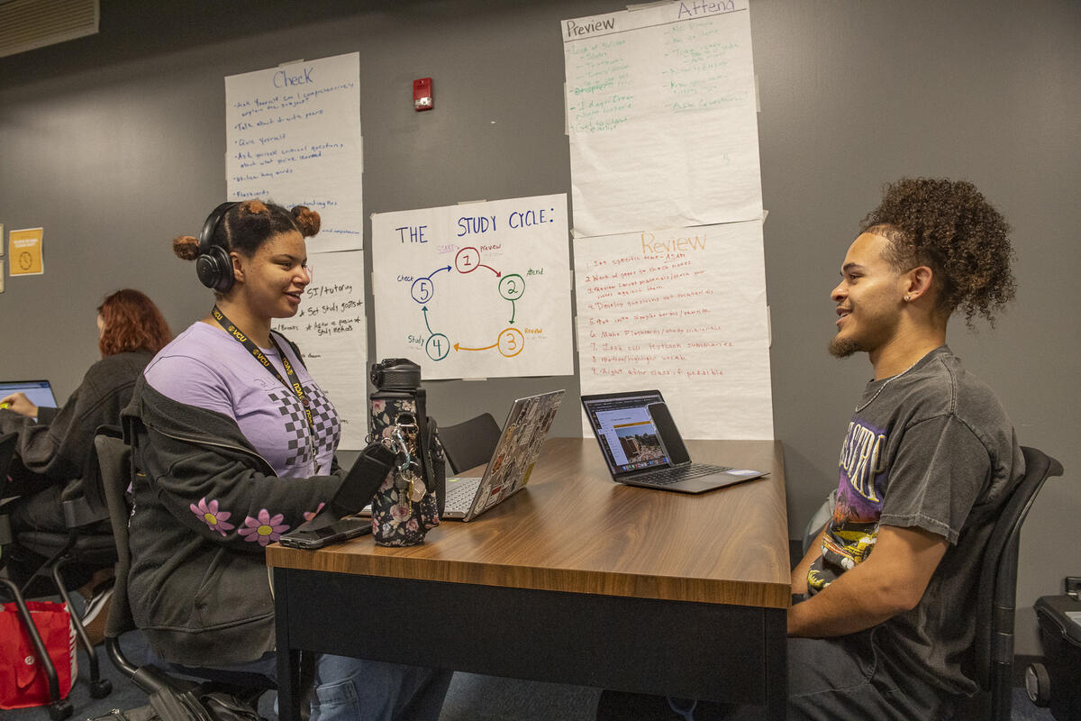 A photo of two people sitting across from each other at a table with laptops sitting on the table 