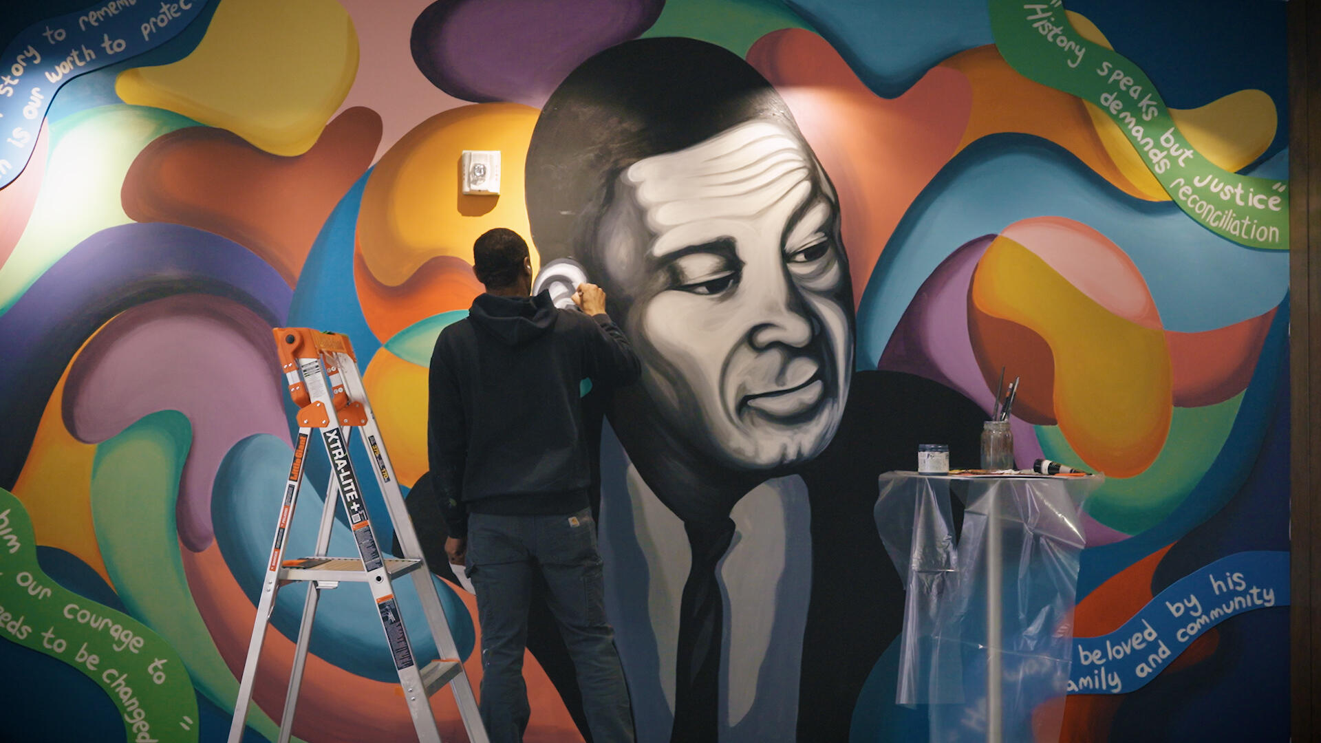 A man paints a colorful mural on a wall.