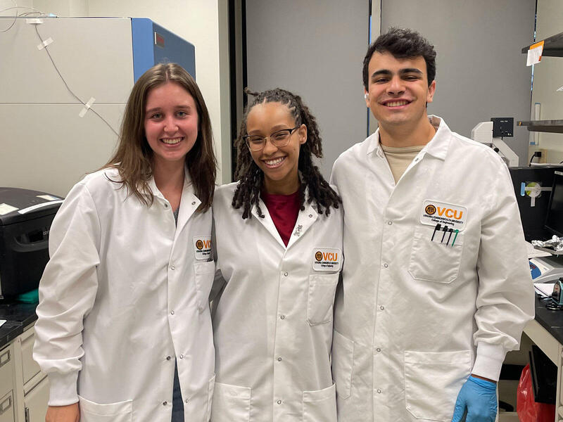 A photo of three people wearing white lab coats standing and smiling. 