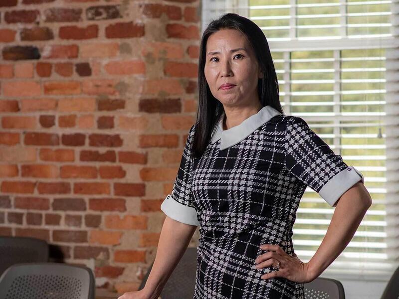 A portrait of a woman with one hand on her hip and the other resting on a chair. 