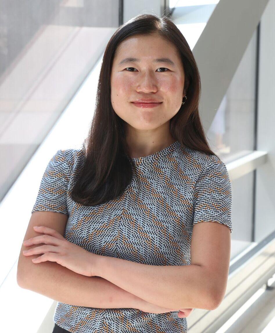A photo of a woman from the waist up. She is smiling and her arms are crossed against her chest. 
