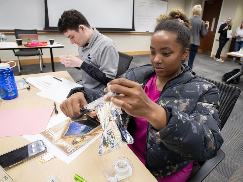 A photo of two students sitting at a table doing crafting activities. 