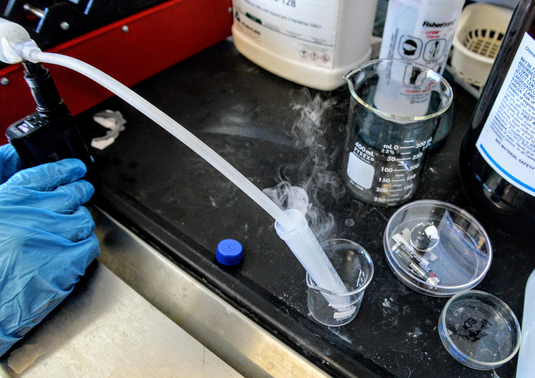 E-cigarette vapor rises from a beaker while researcher Suraj Kandalam demonstrates the use of a pump meant to simulate e-cigarette smoking and to create solutions used in testing.
<br>Photo by Leah Small, University Public Affairs


