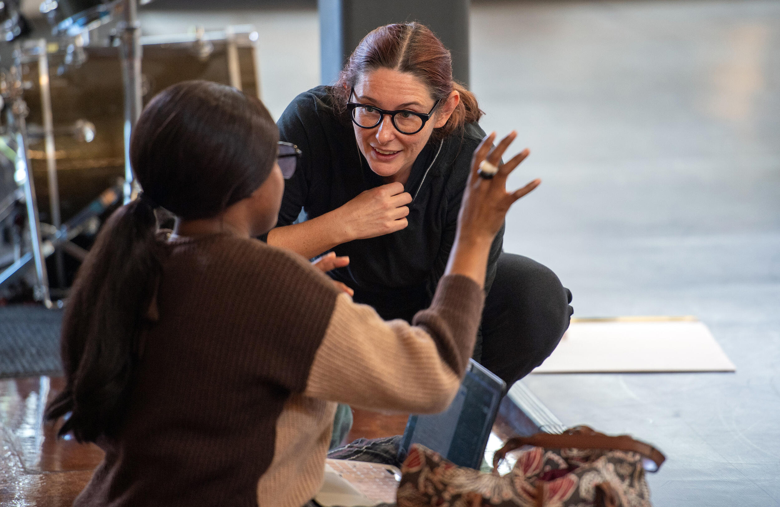 A photo of two women talking to each other while sitting and kneeling on the floor. 