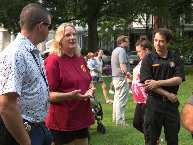 A photo of three people in a circle talking in a public park. Other people are walking around the park in the background. 