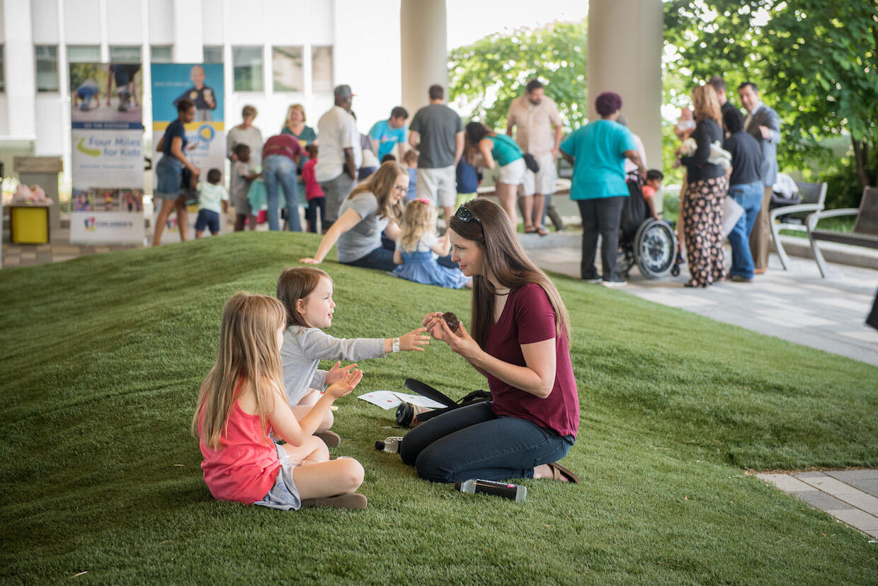 A woman and two young girls share a snack while sitting outside.