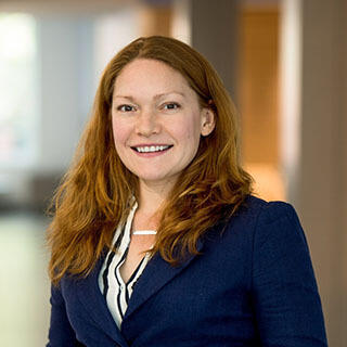 A portrait of a woman wearing a navy blue sportscoat and a white shirt with navy blue stripes. 