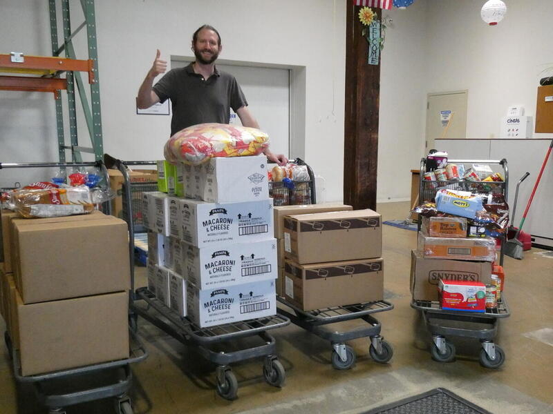 A man standing behind four trollies filled with boxes of food. 