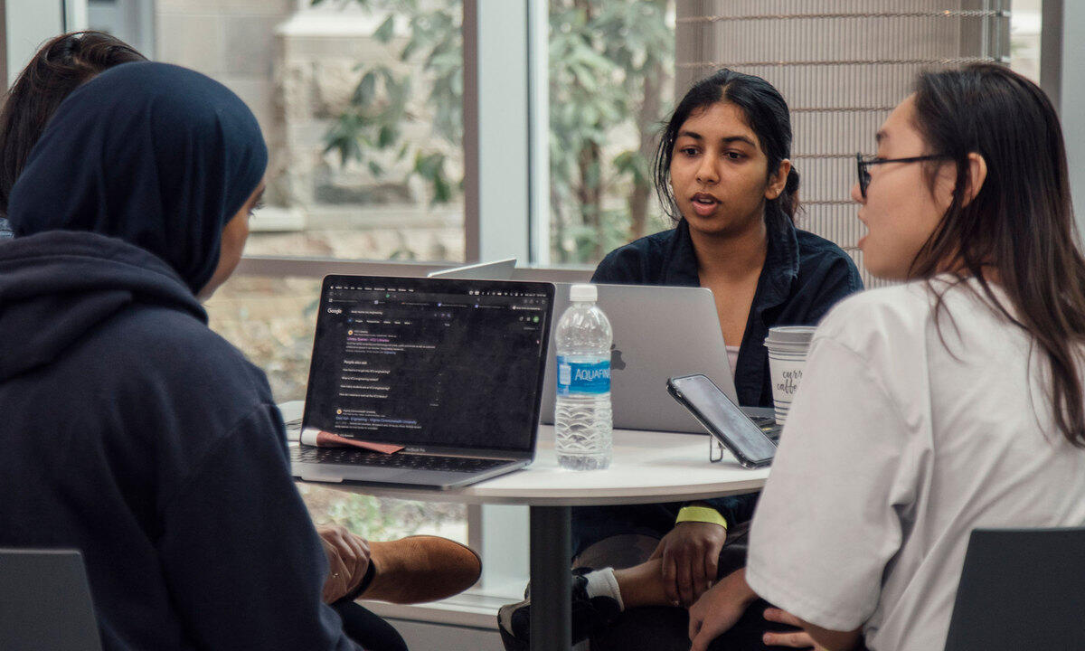 A photo of four people sitting at a table with laptops on it. 