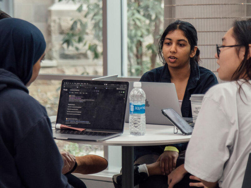 A photo of four people sitting at a table with laptops on it. 