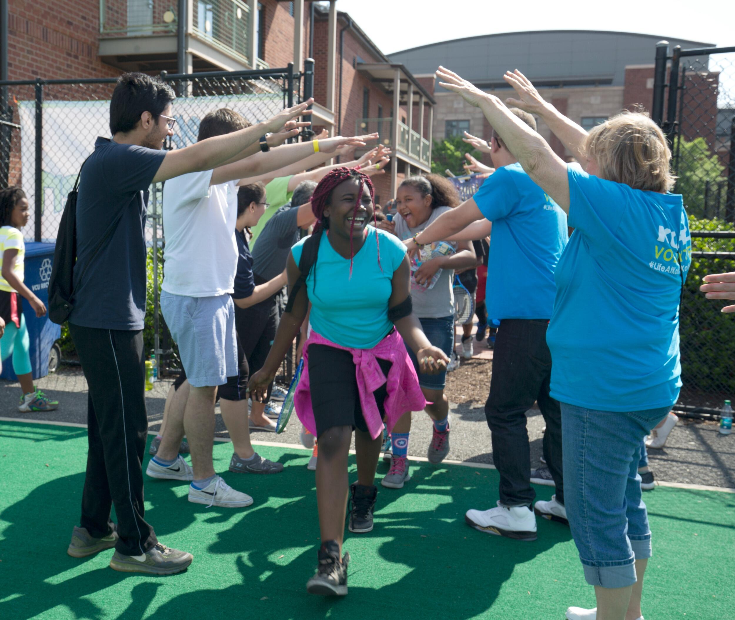 A photo of people with their arms raised in the air forming a tunnel with other people running underneath it. 