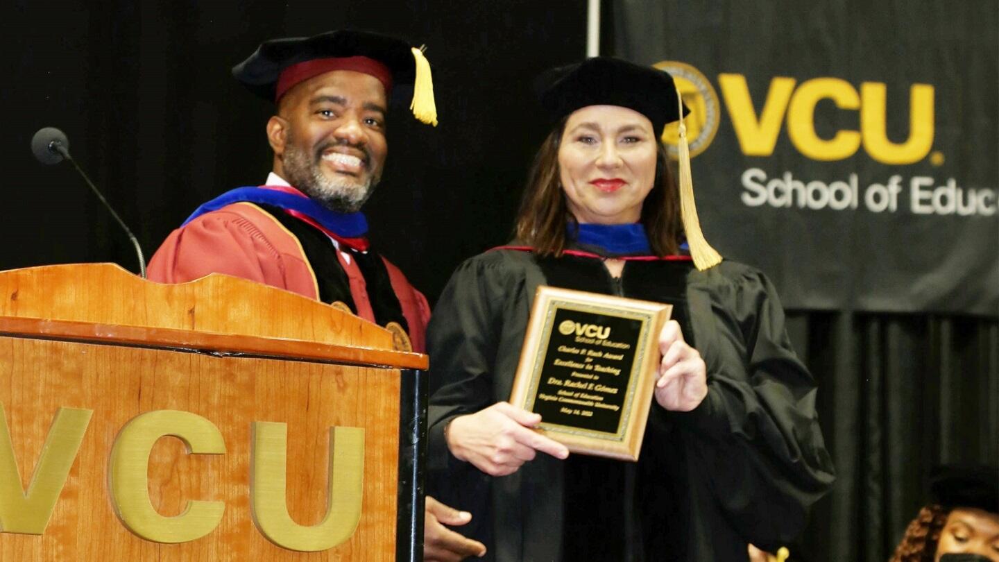 A woman in a graduation cap and gown holding a plaque standing next to a man. 