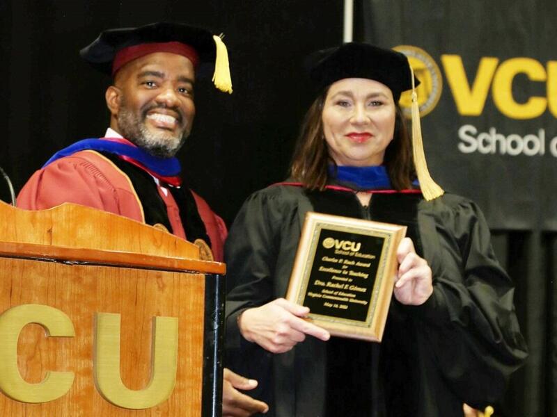 A woman in a graduation cap and gown holding a plaque standing next to a man. 
