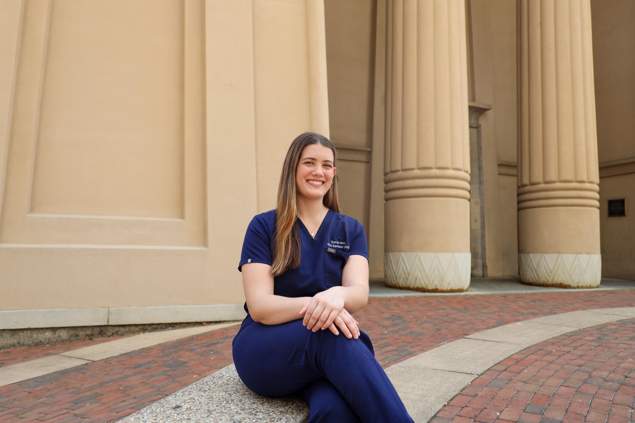 A woman sits with her legs crossed in front of columns.