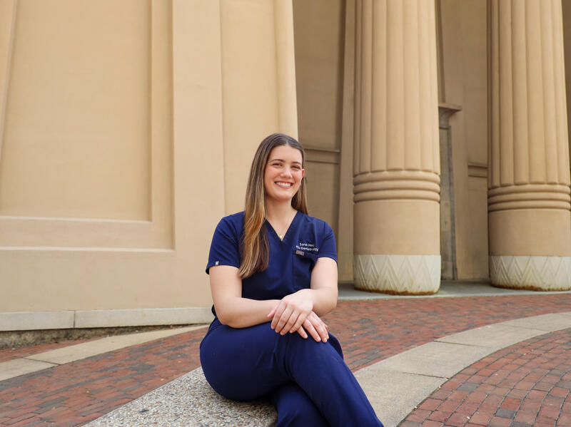 A woman sits with her legs crossed in front of columns.