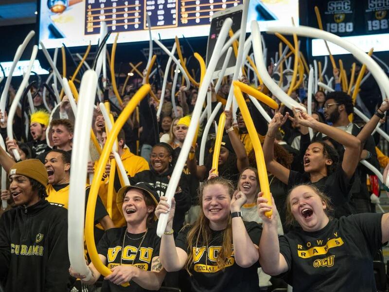 A photo of a crowd of people waving long balloons and cheering. 