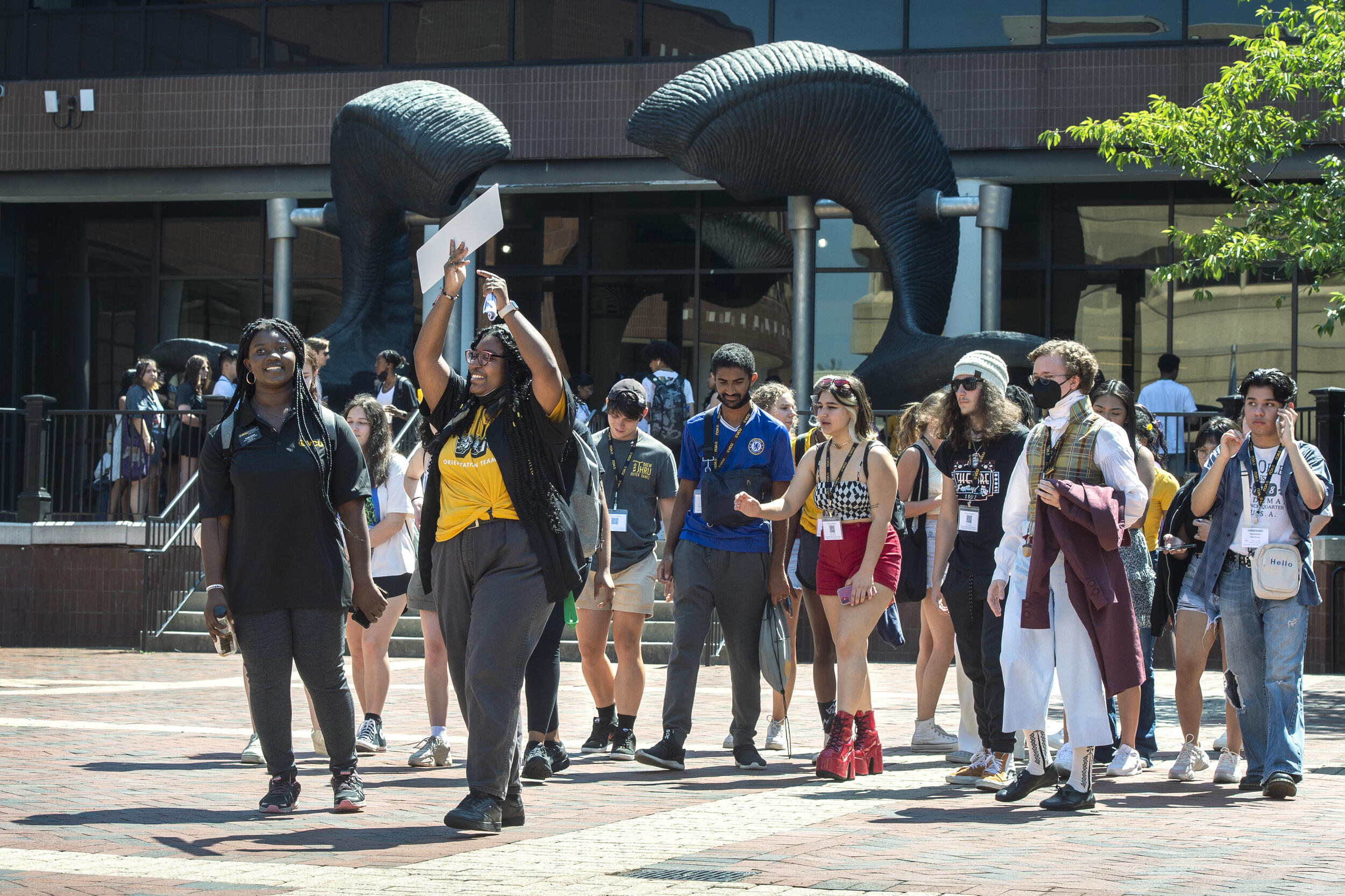 A group of people walking by the ram horns statue outside of the University Student Commons. 