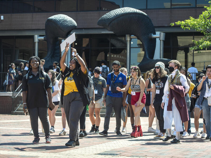 A group of people walking by the ram horns statue outside of the University Student Commons. 