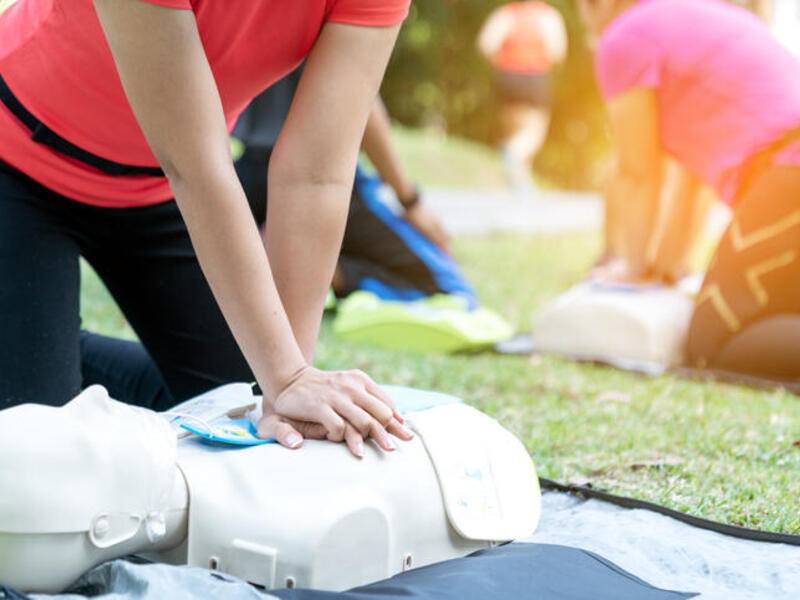 Two people pressing their hands down on the chest of a CPR practice dummy. 