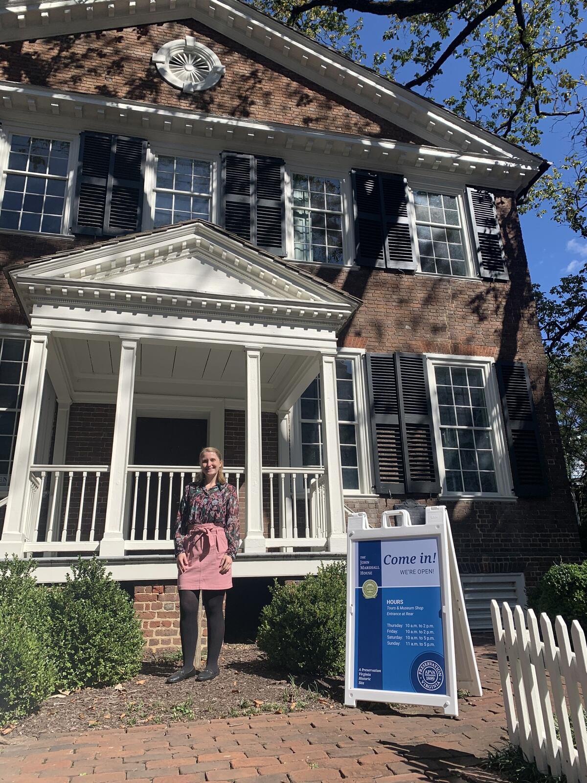 A woman stands in front of the front porch of a house.