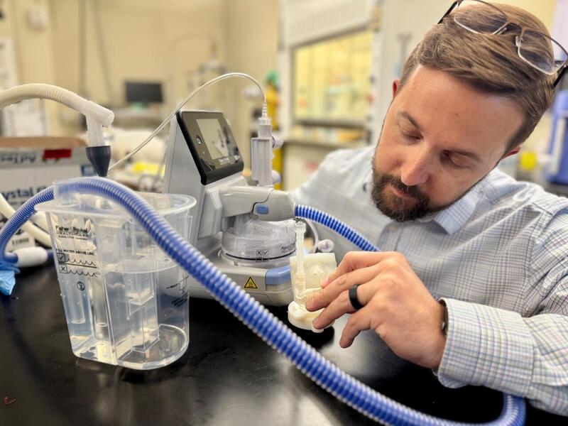 A photo of a man sitting at a table looking at a machine. 