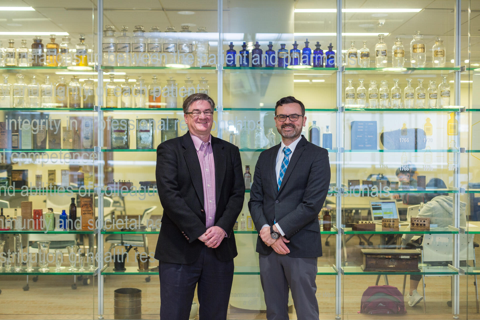 Two people in business suits standing in front of a glass wall.
