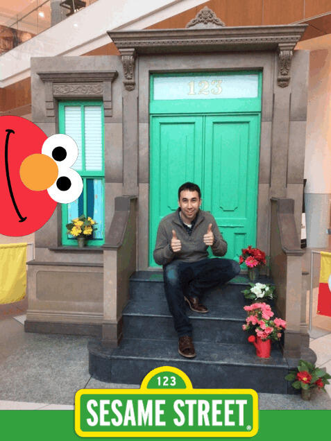 A photo of a man sitting on a fake stoop for a home. 
